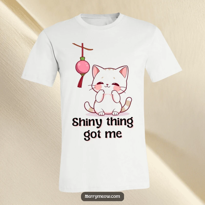 Funny t-shirt showcasing a mischievous cat character enthusiastically batting at a shiny, dangling Christmas ornament, capturing festive feline antics.
